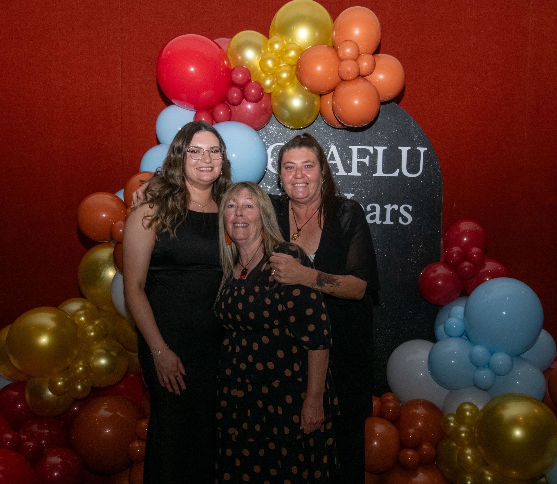 CAAFLU women posing, smiling in front of a balloon arch at an event.