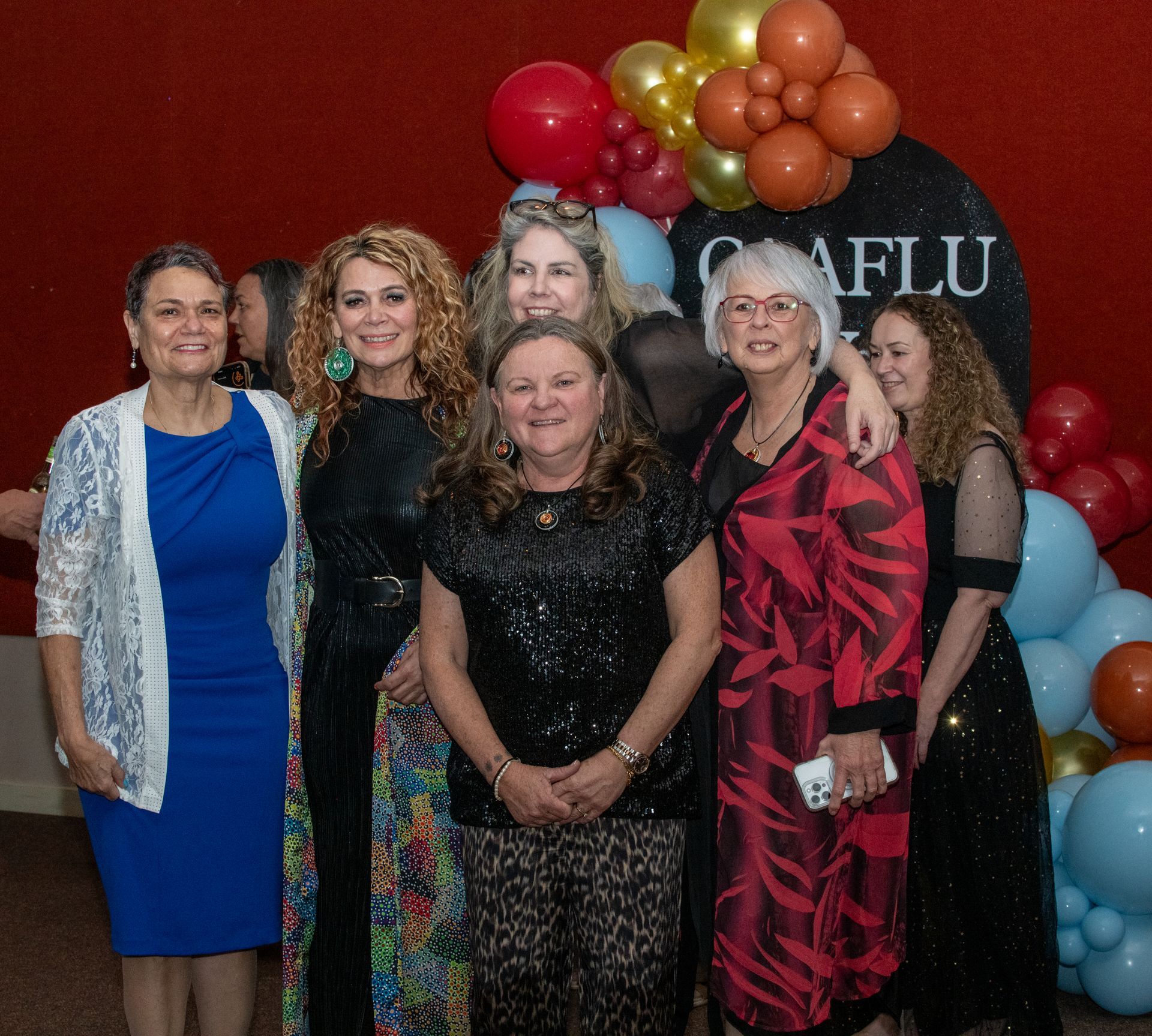 CAAFLU women smiling, posing at a formal event with balloons and a logo in the background.