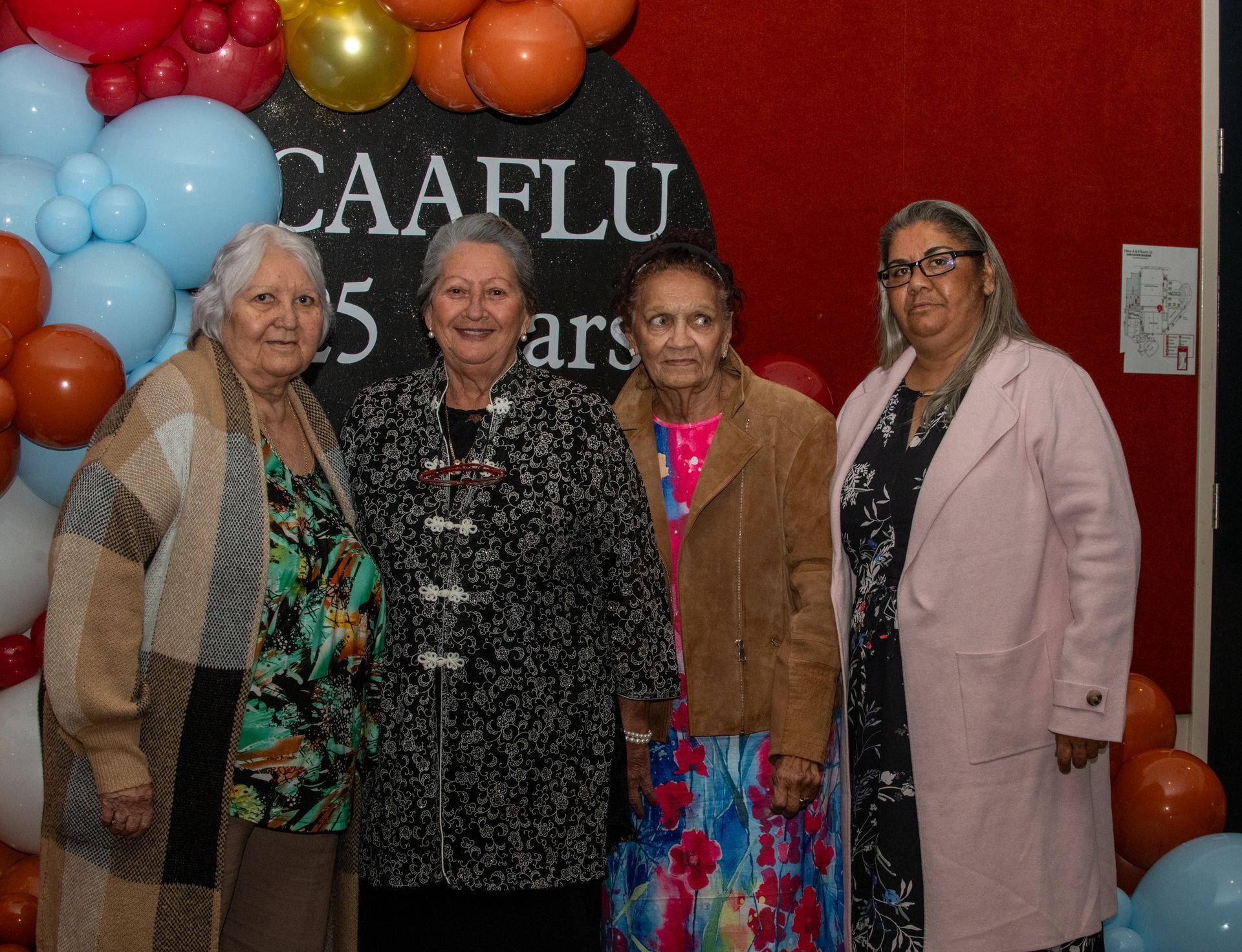 Four women smiling, posing in front of a balloon arch, celebrating 
