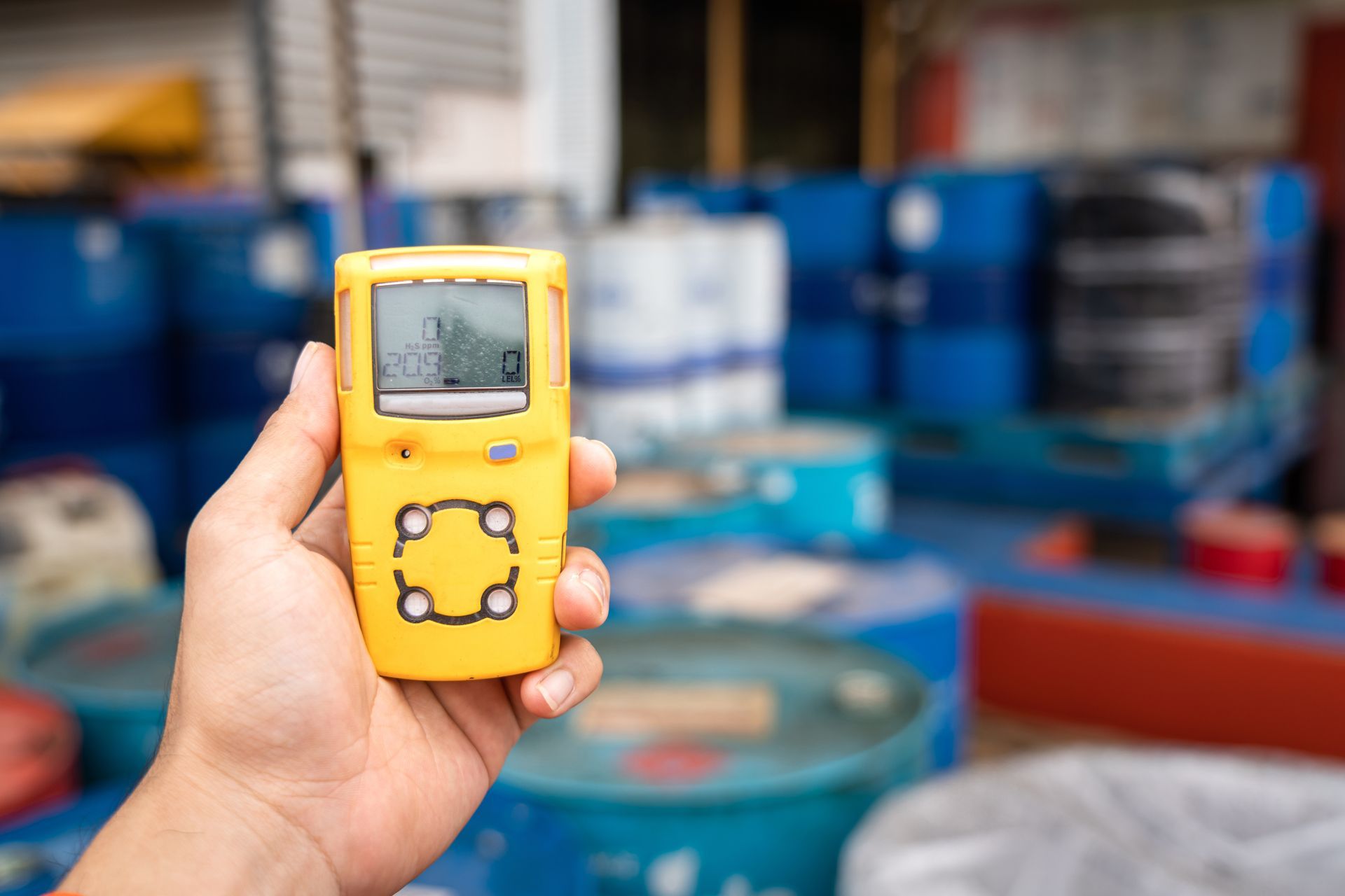 A hand holding a yellow portable gas detector to monitor the air around a chemical storage area. A hand holding a yellow portable gas detector to monitor the air around a chemical storage area.