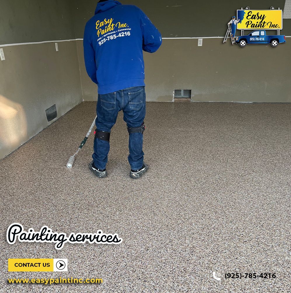 A person in blue applies epoxy coating to a garage floor.