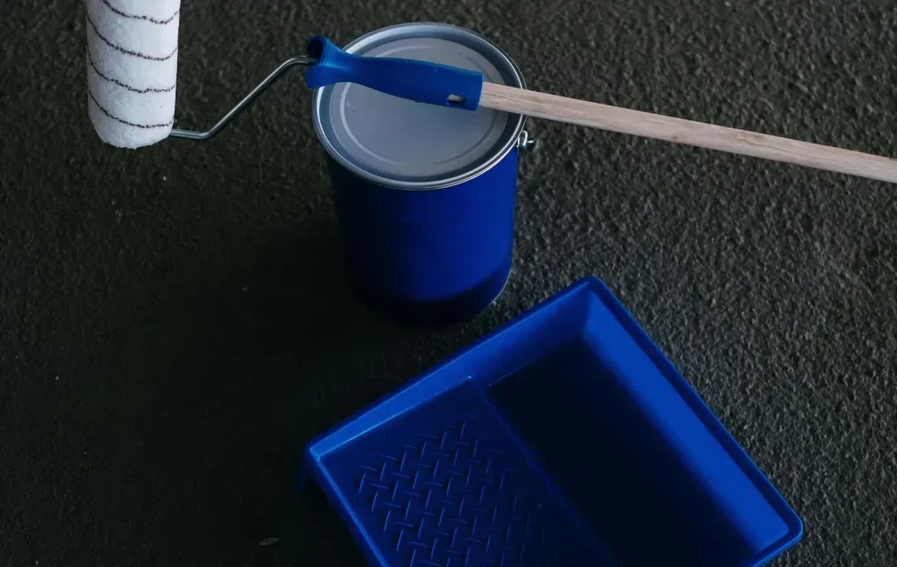Paint roller, blue paint can, and tray on a dark surface, ready for painting.