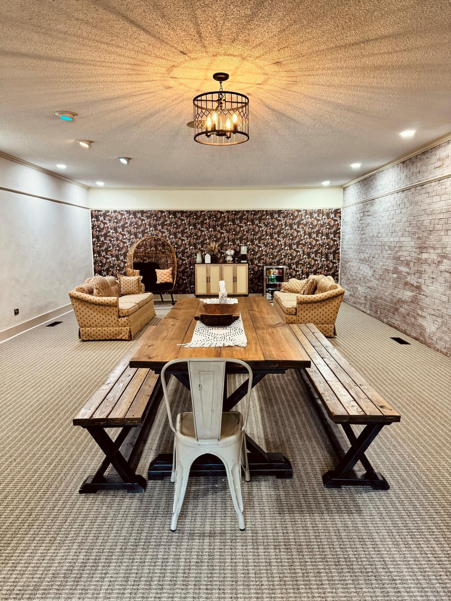 Indoor lounge with a long wooden table, benches, chairs, and wicker sofas on a patterned carpet