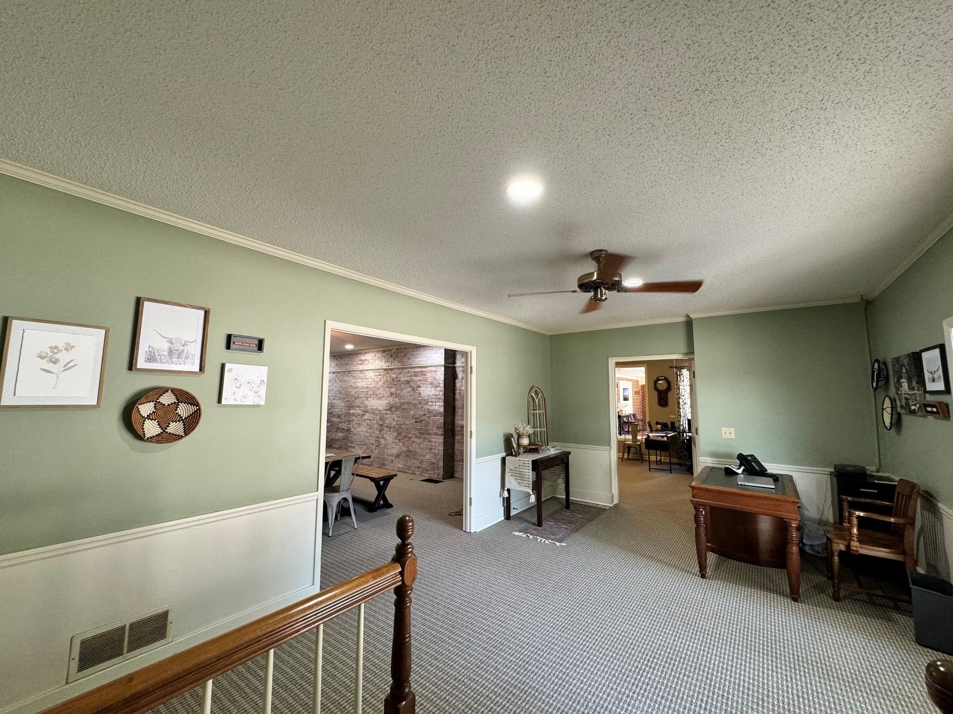 Living room with green walls, carpet, ceiling fan, open doorway, and desk by the window.