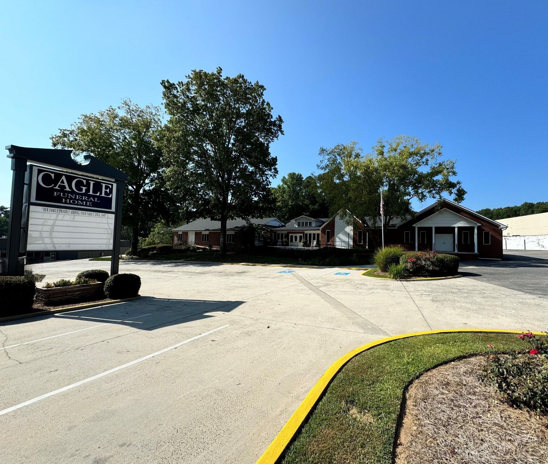Church campus entrance with sign, paved driveway, trees, and small buildings under a blue sky