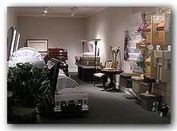 Cluttered storage room with stacked boxes, furniture, and household items under fluorescent lights