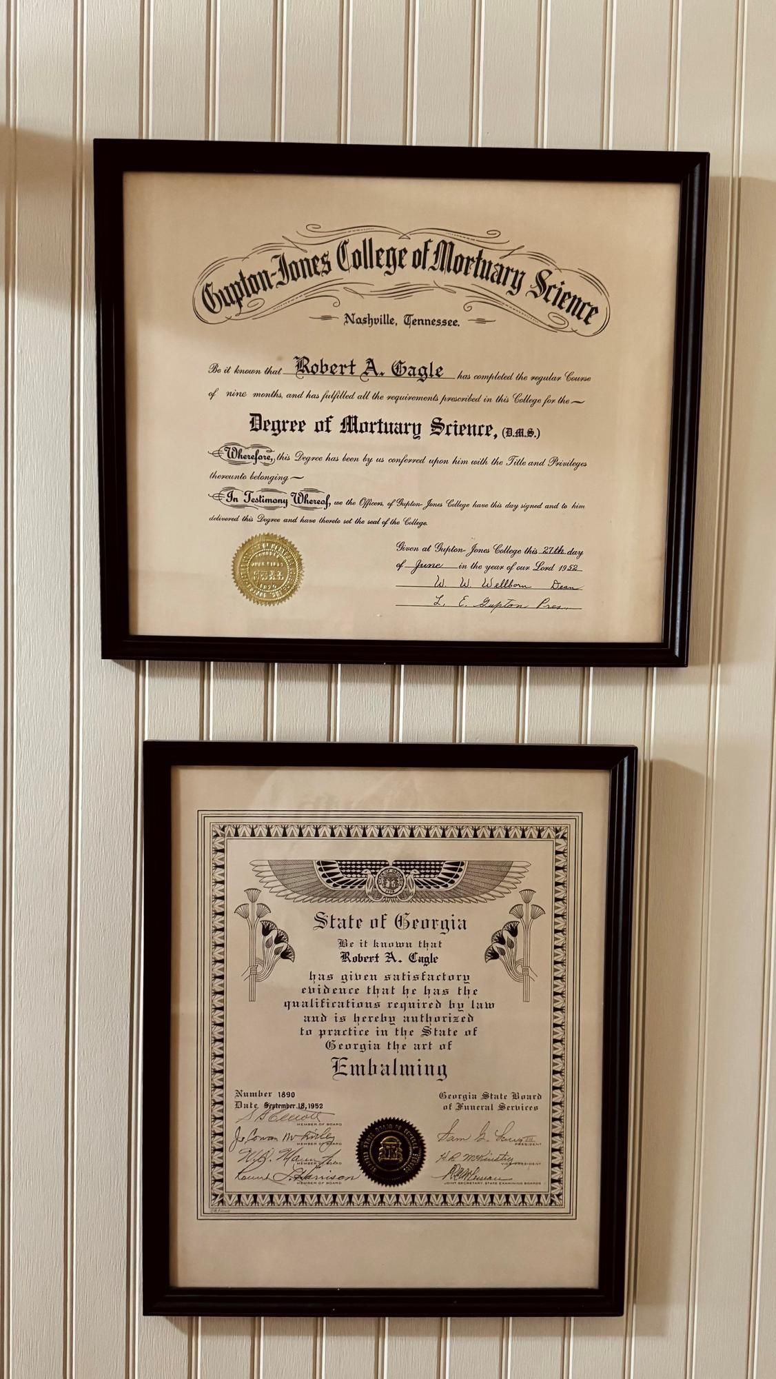 Two framed certificates with cream paper and dark borders hanging on a striped wall.