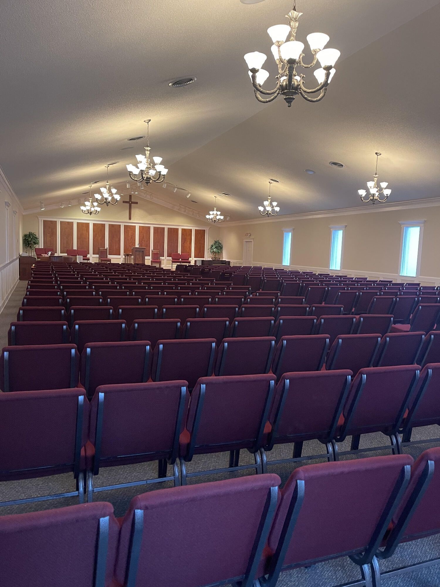 Empty church hall with rows of purple chairs and chandeliers under a vaulted ceiling.