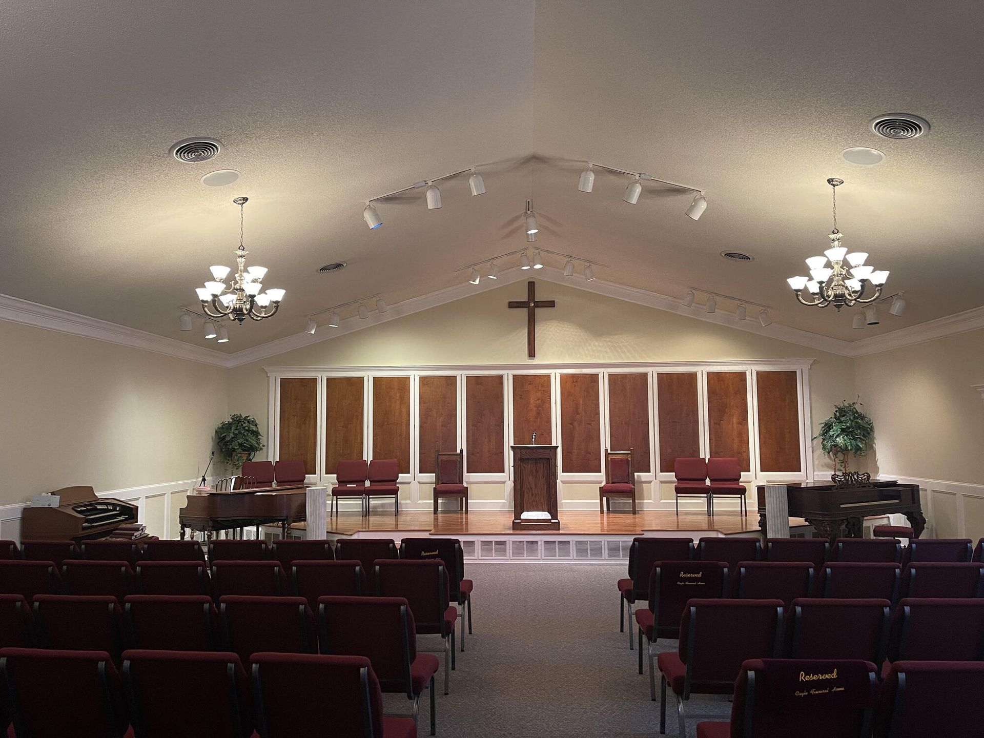 Church sanctuary with rows of pews, a central cross, and a raised altar under chandelier lights.