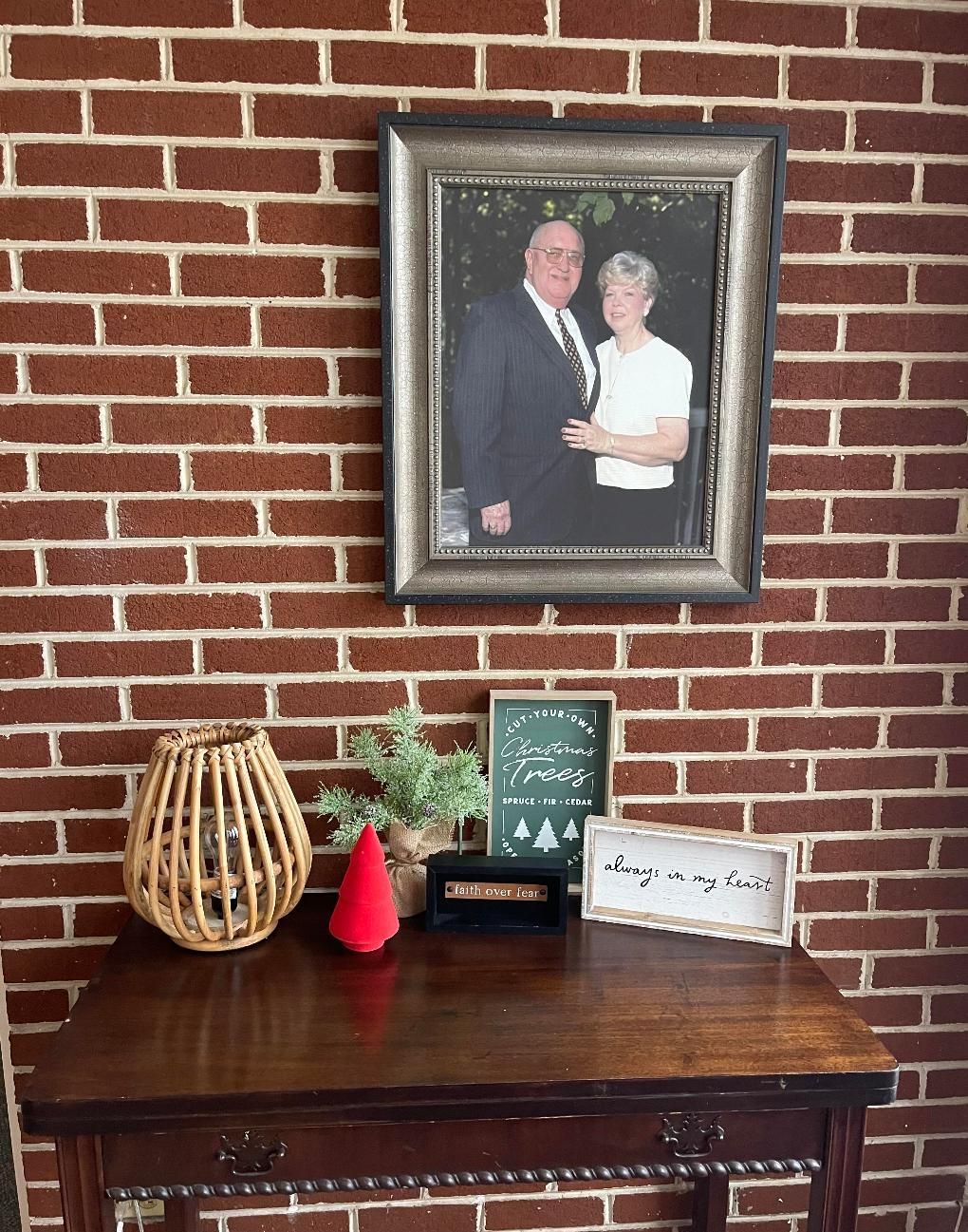 Framed couple portrait above a wooden table with decorative items against a red brick wall