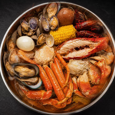 Seafood boil in a pot with crab, shrimp, corn, sausage, eggs, and mussels in red broth