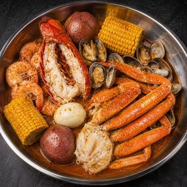 Seafood boil with crab legs, corn, potatoes, sausage, shrimp, and clams in a metal tray