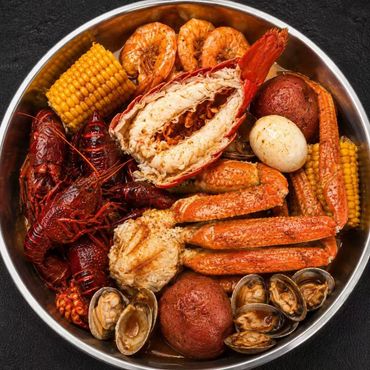 Seafood boil platter with crab legs, shrimp, corn, sausage, potatoes, and clams in a metal bowl