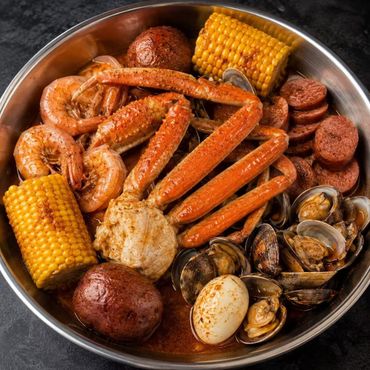 Seafood boil with shrimp, crab legs, sausage, potatoes, corn, and clams in a metal tray