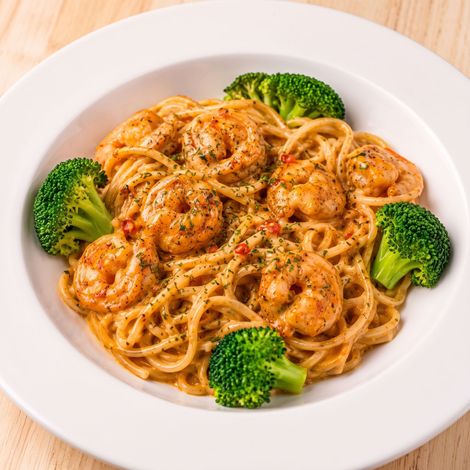 White plate of shrimp pasta with broccoli florets on a light background