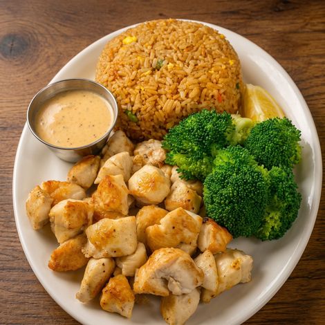 Plated chicken with rice, broccoli, lemon wedge, and dipping sauce on a white dish