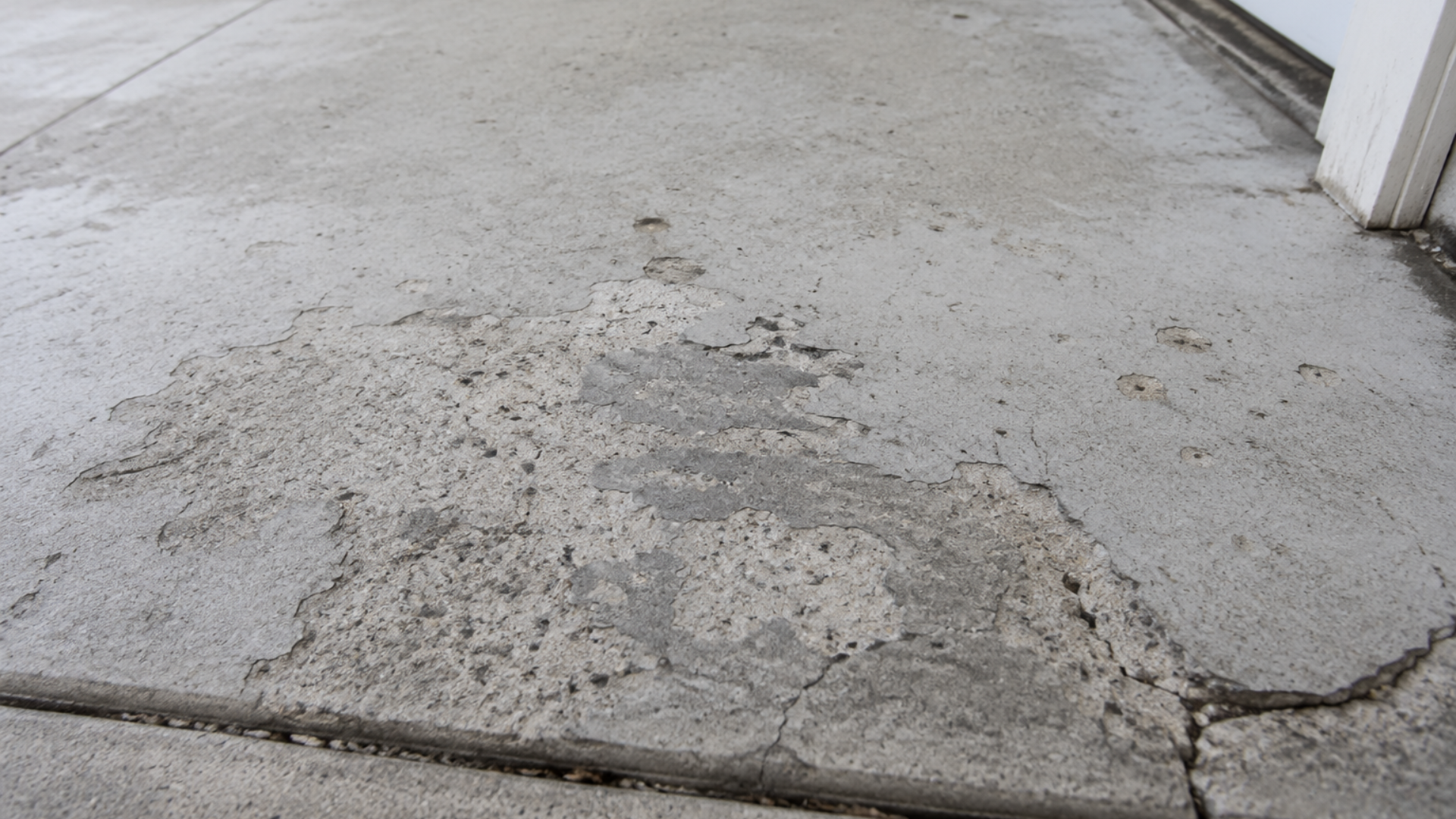 Cracked, uneven concrete floor with a large patch of damaged pavement near a wall.