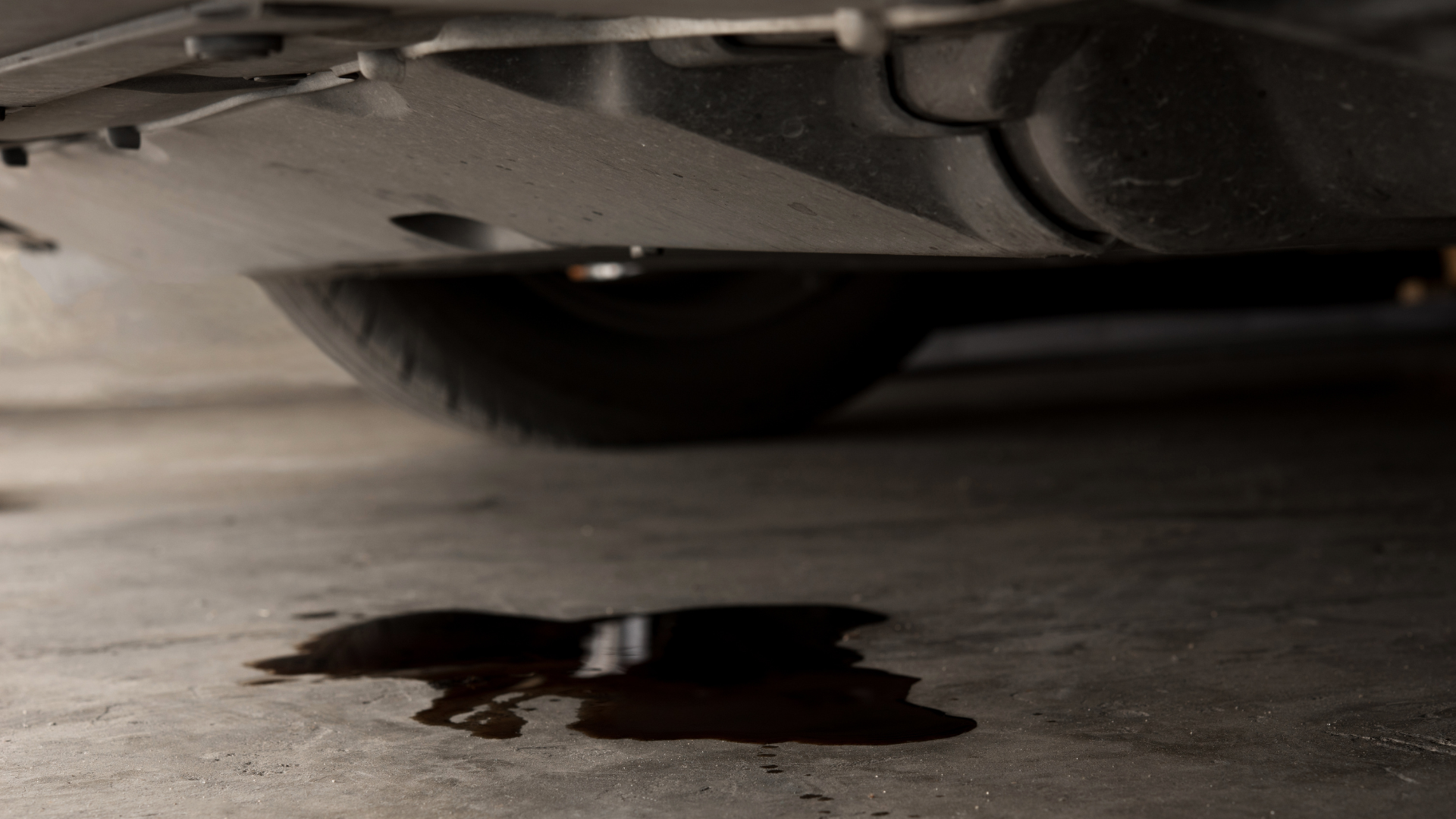 Dark red liquid puddle under a parked car on a concrete floor