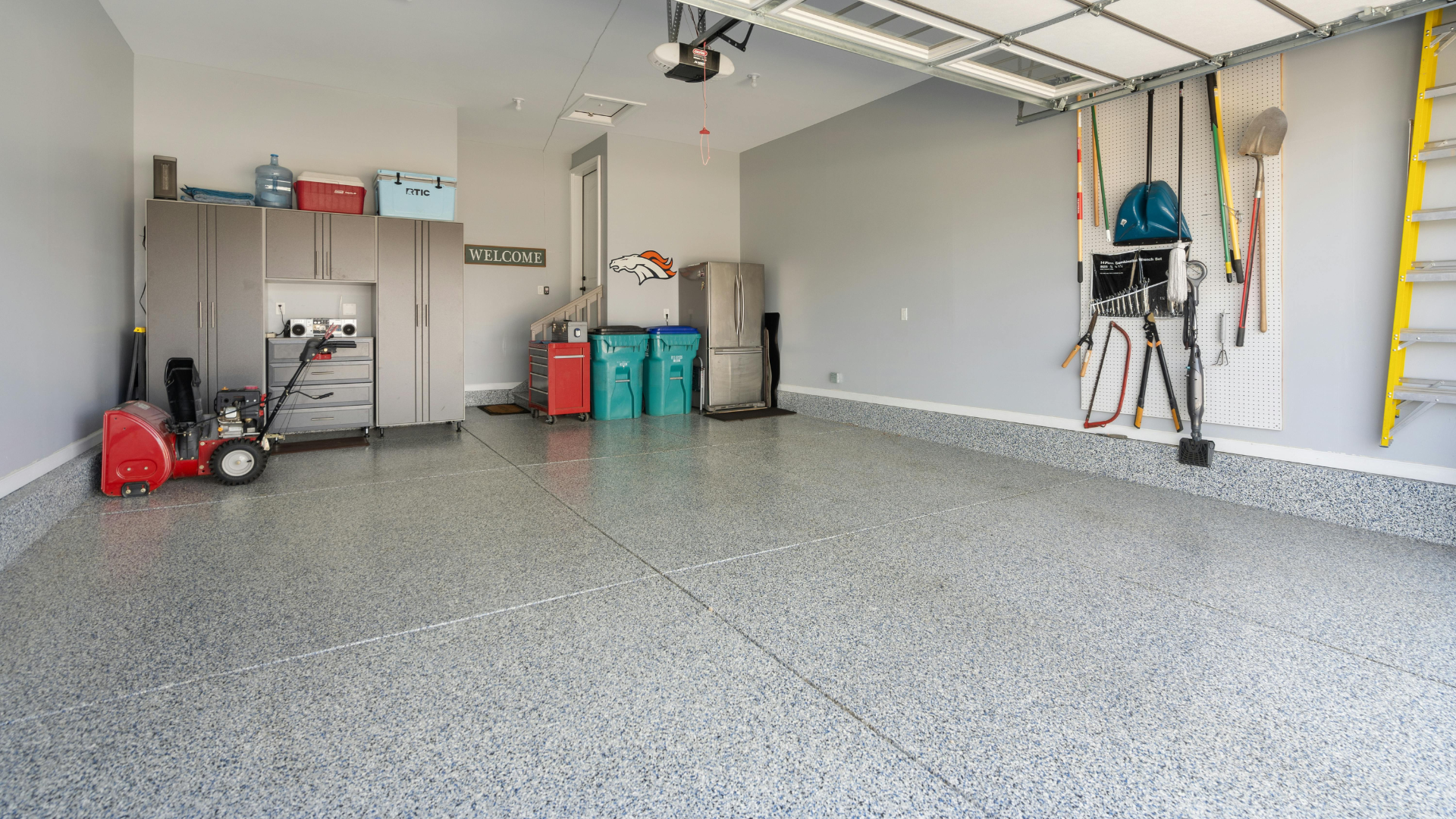 Spacious garage with speckled floor, storage bins, tools, bicycles, and a closed overhead door