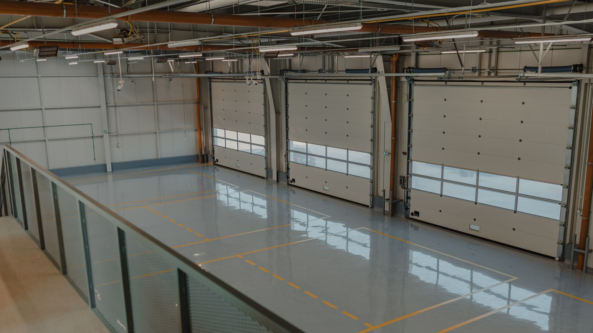 Empty indoor industrial bay with polished concrete floor, large overhead doors, and exposed ceiling beams