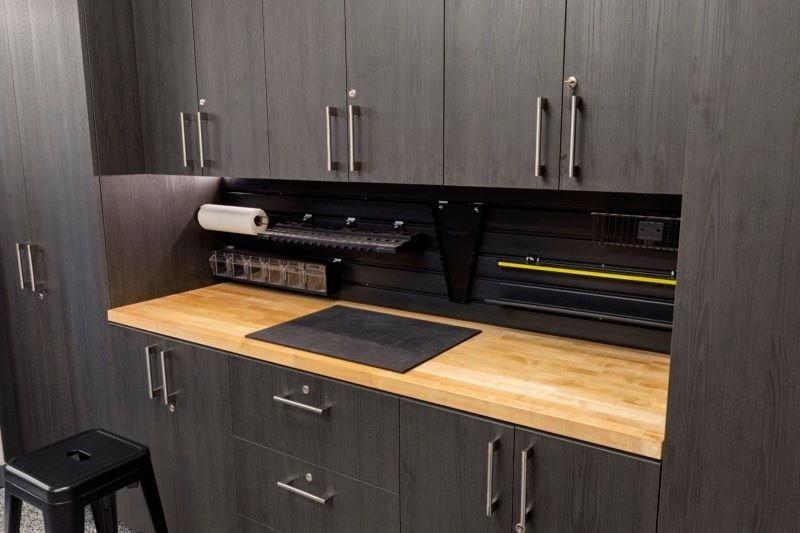 Modern craft workspace with dark cabinets, wood countertop, and a desktop cutting machine under wall cabinets