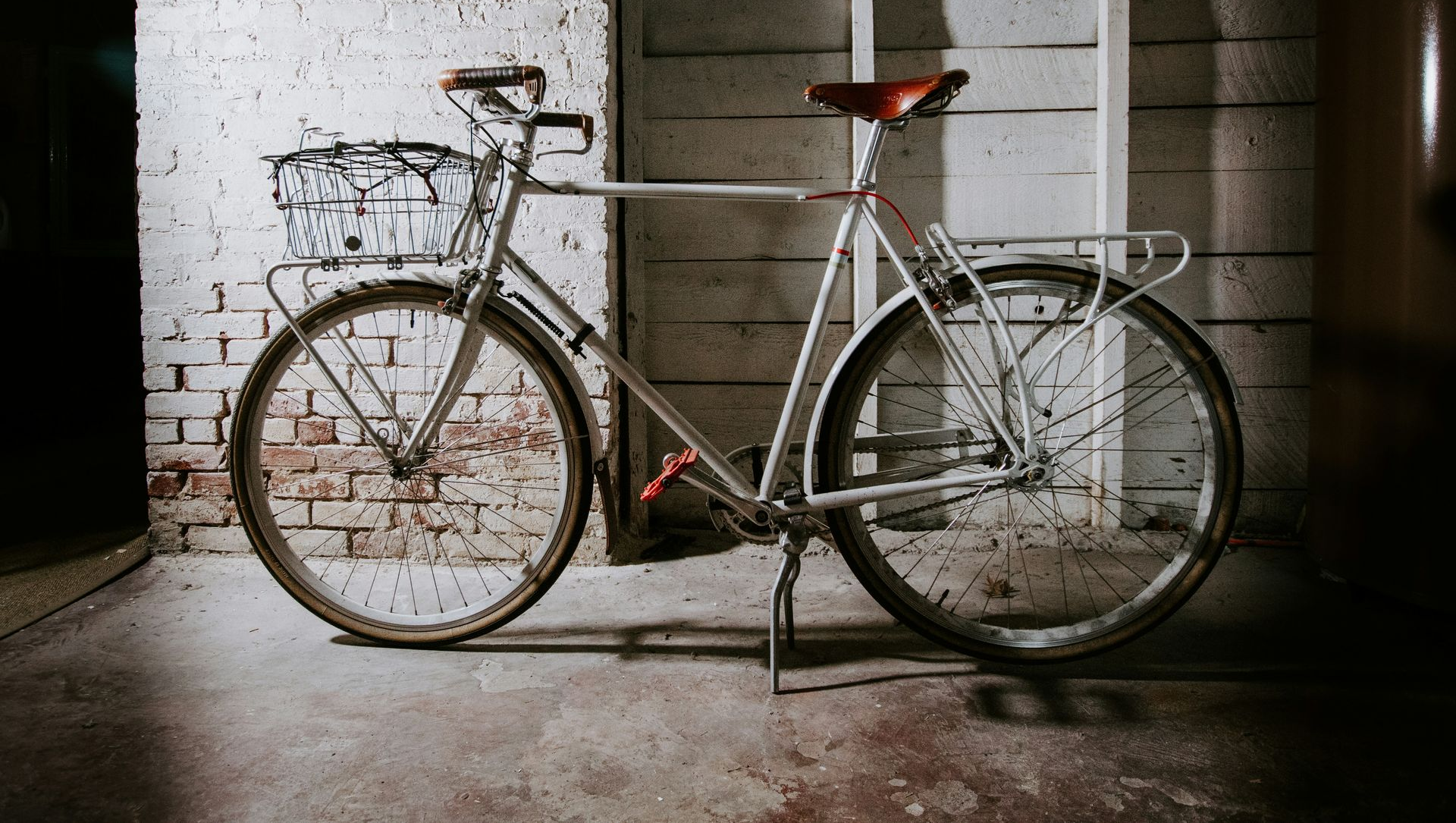 Vintage silver bicycle with a rear rack parked against a brick wall in a dim garage