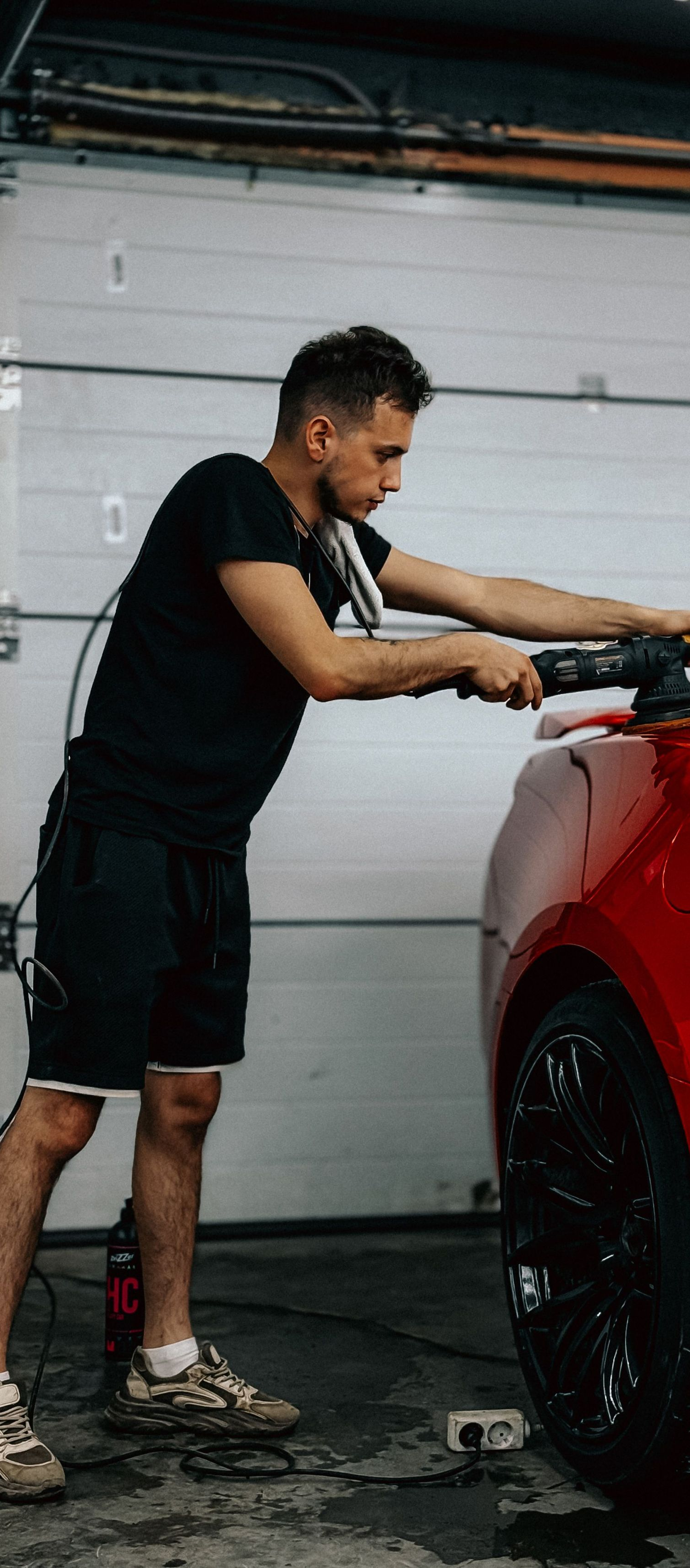 Man polishing a red car in a garage with a cloth and spray bottle