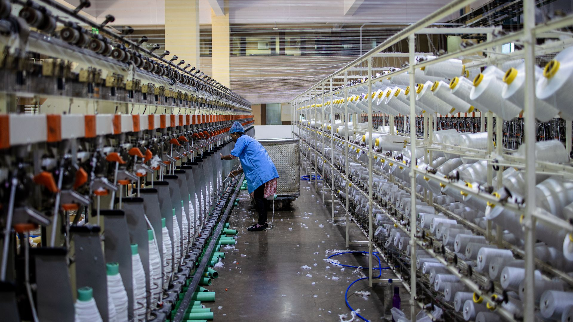 Worker tending rows of yarn spools in a textile factory