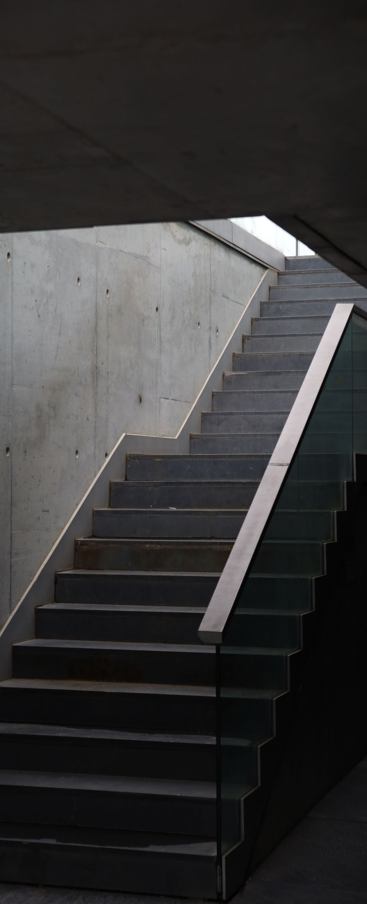 Concrete staircase under a low ceiling, leading upward in a dim, modern interior.