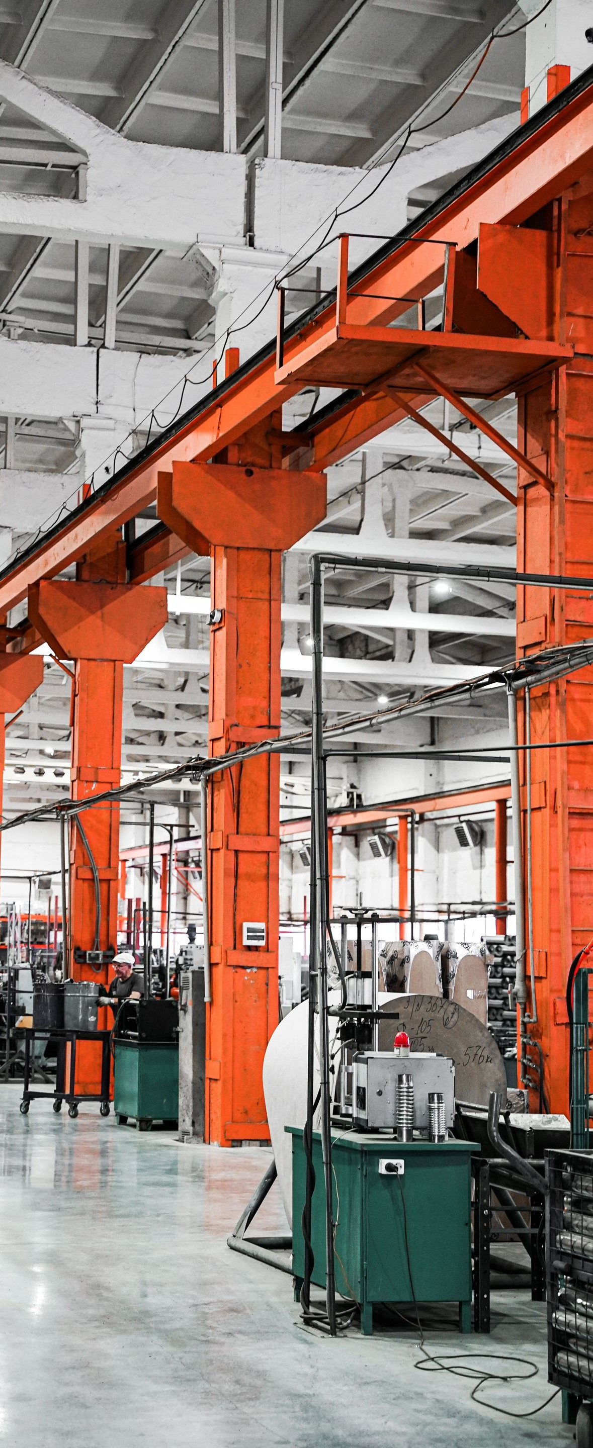 Orange industrial machinery in a factory with steel beams and overhead equipment