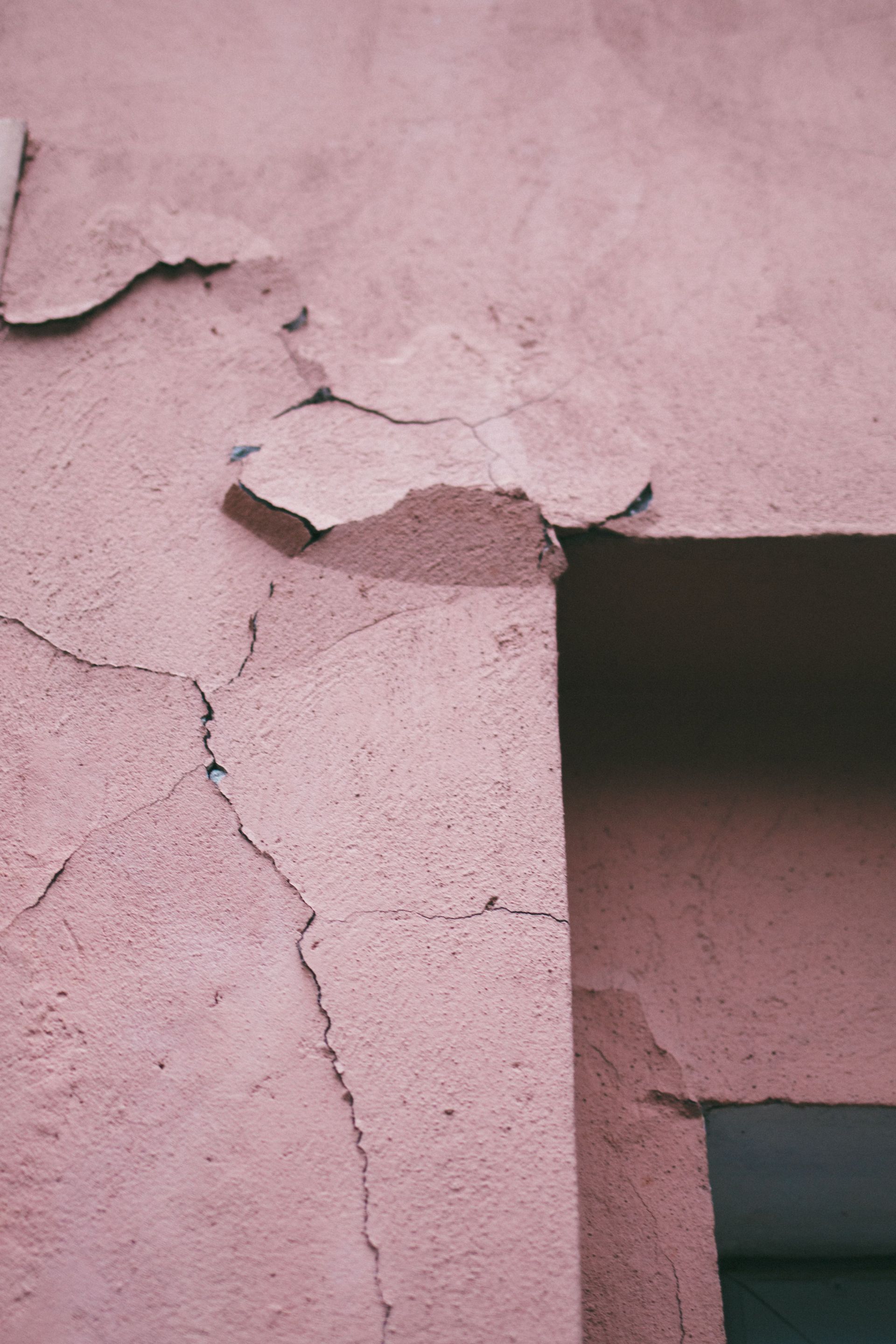 Cracked pink stucco wall with peeling plaster and a dark rectangular opening