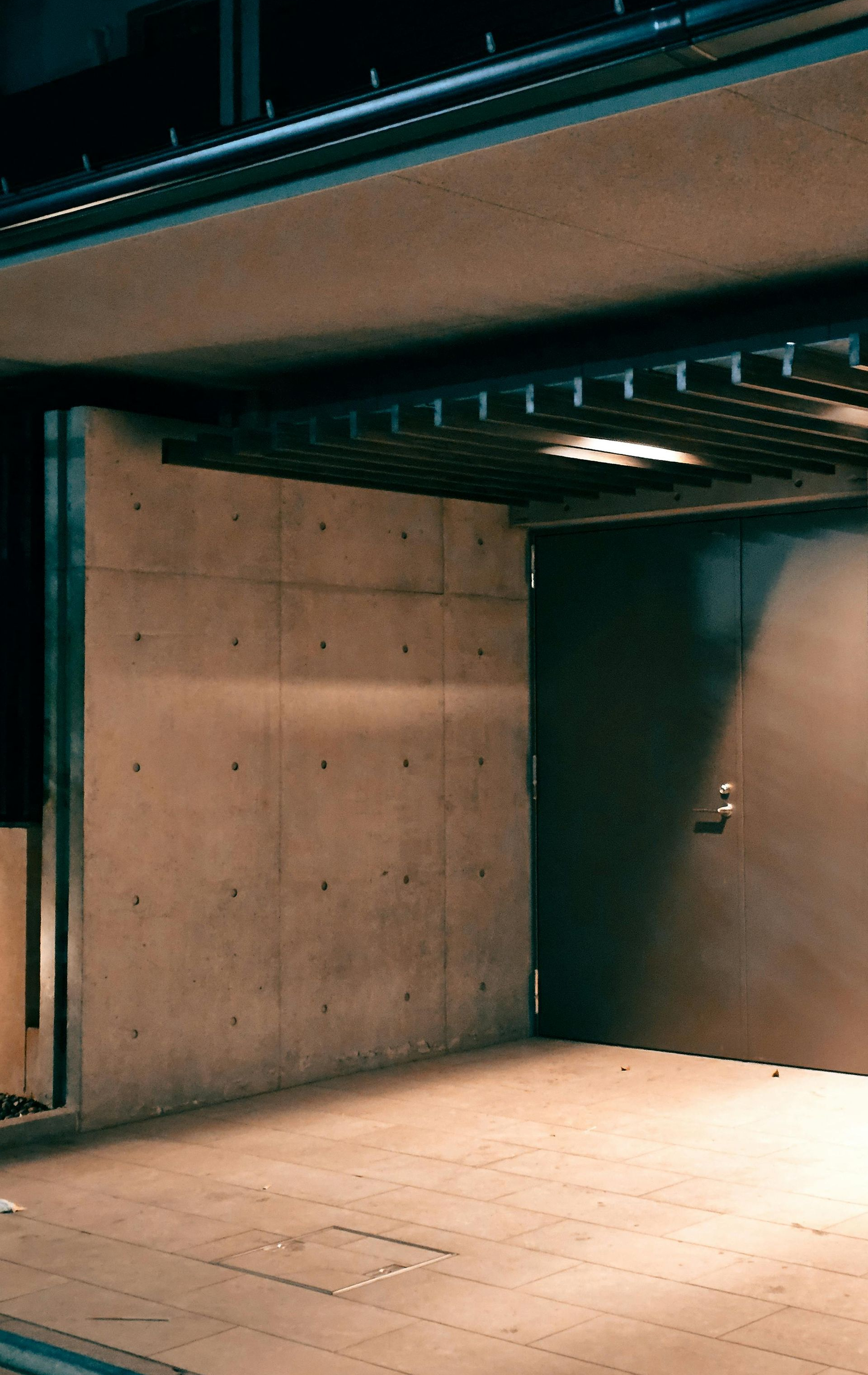 Empty concrete interior with a tiled floor and a dark doorway under exposed beams.