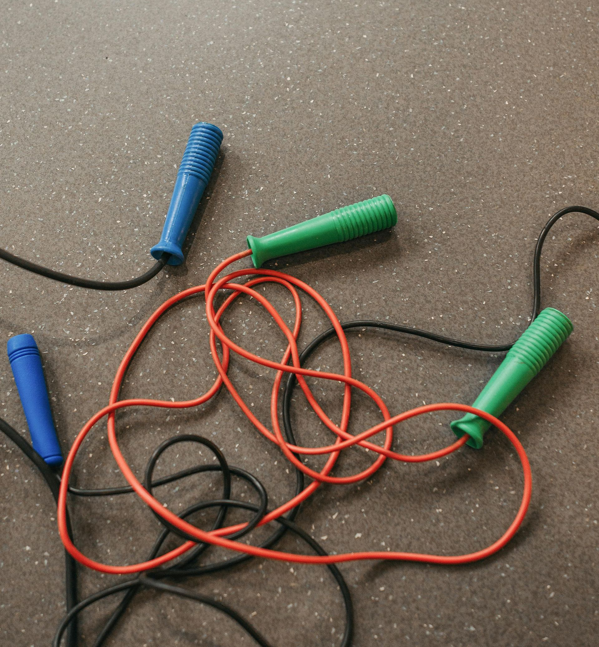 Colorful jump ropes tangled on a brown floor, with blue, green, and orange handles