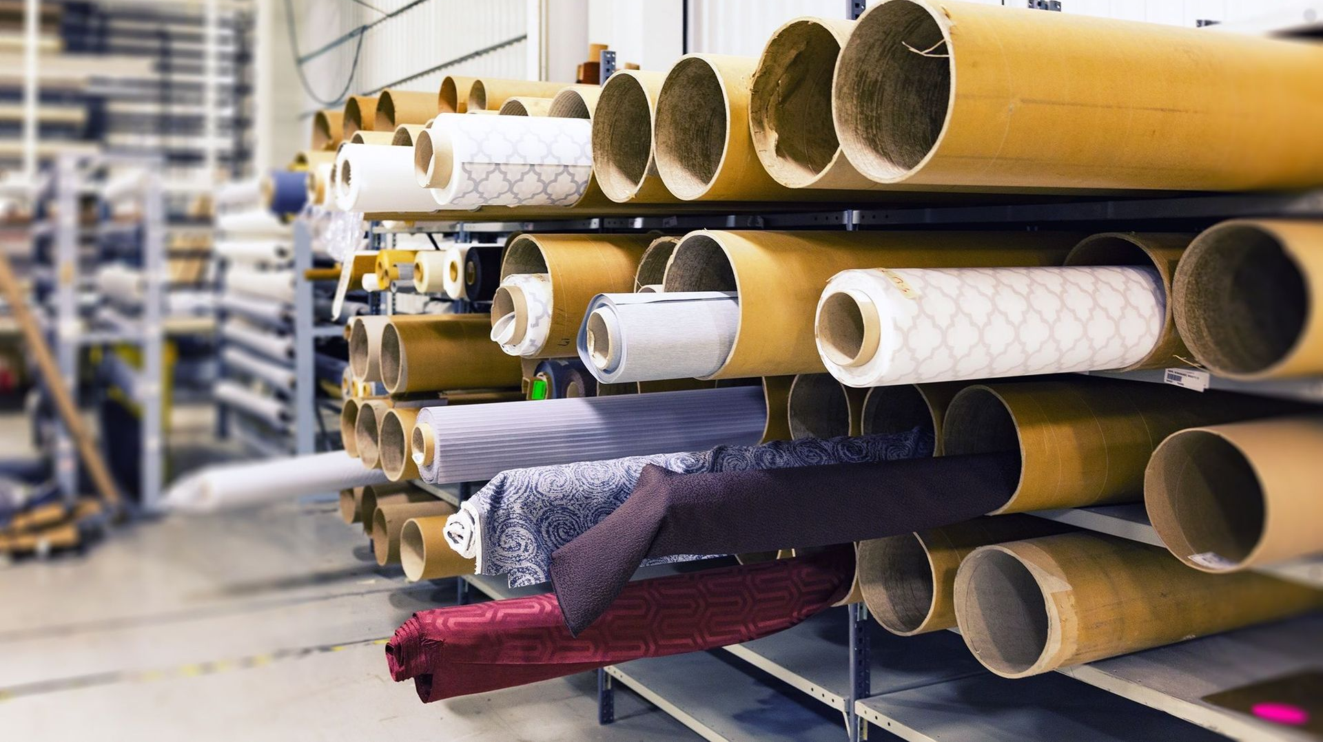 Stacks of rolled carpets and rugs stored on metal racks in a warehouse
