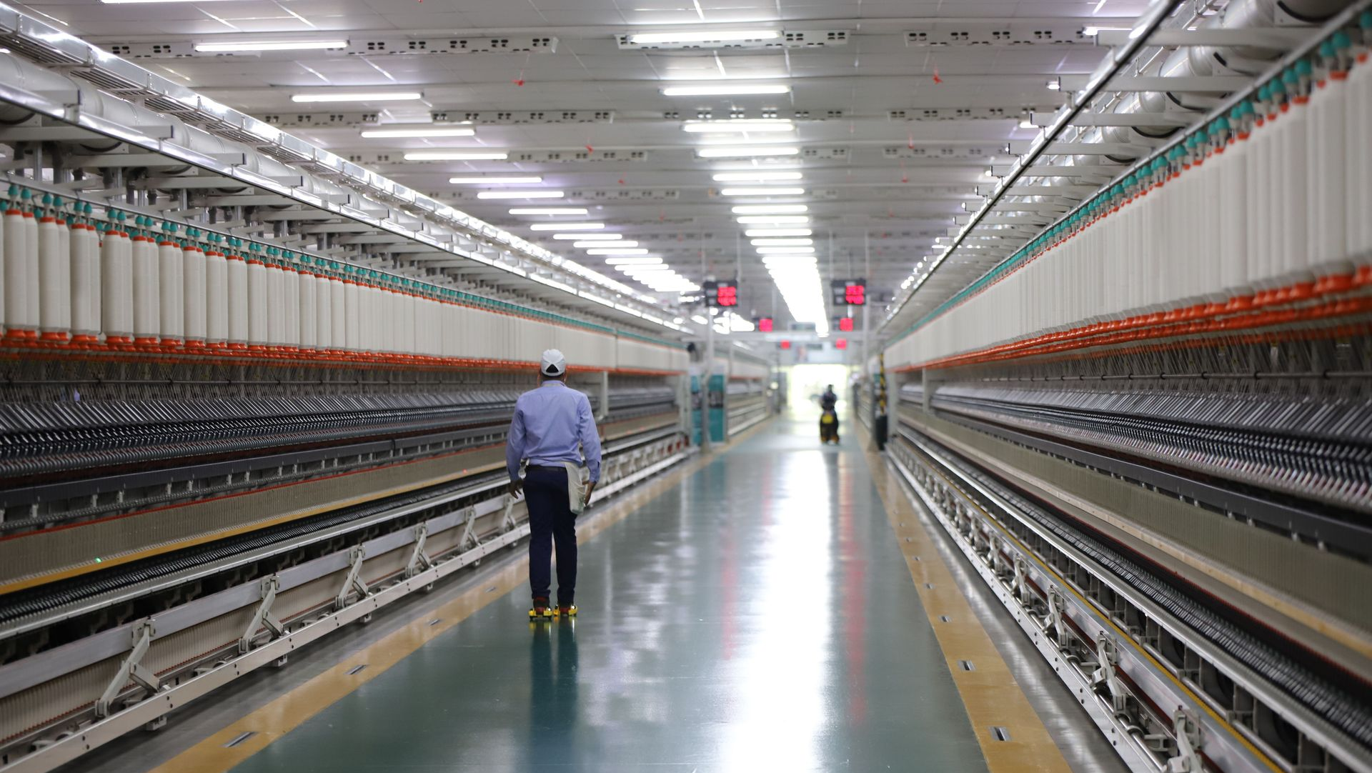 Long factory aisle with a worker walking between rows of machinery and cables