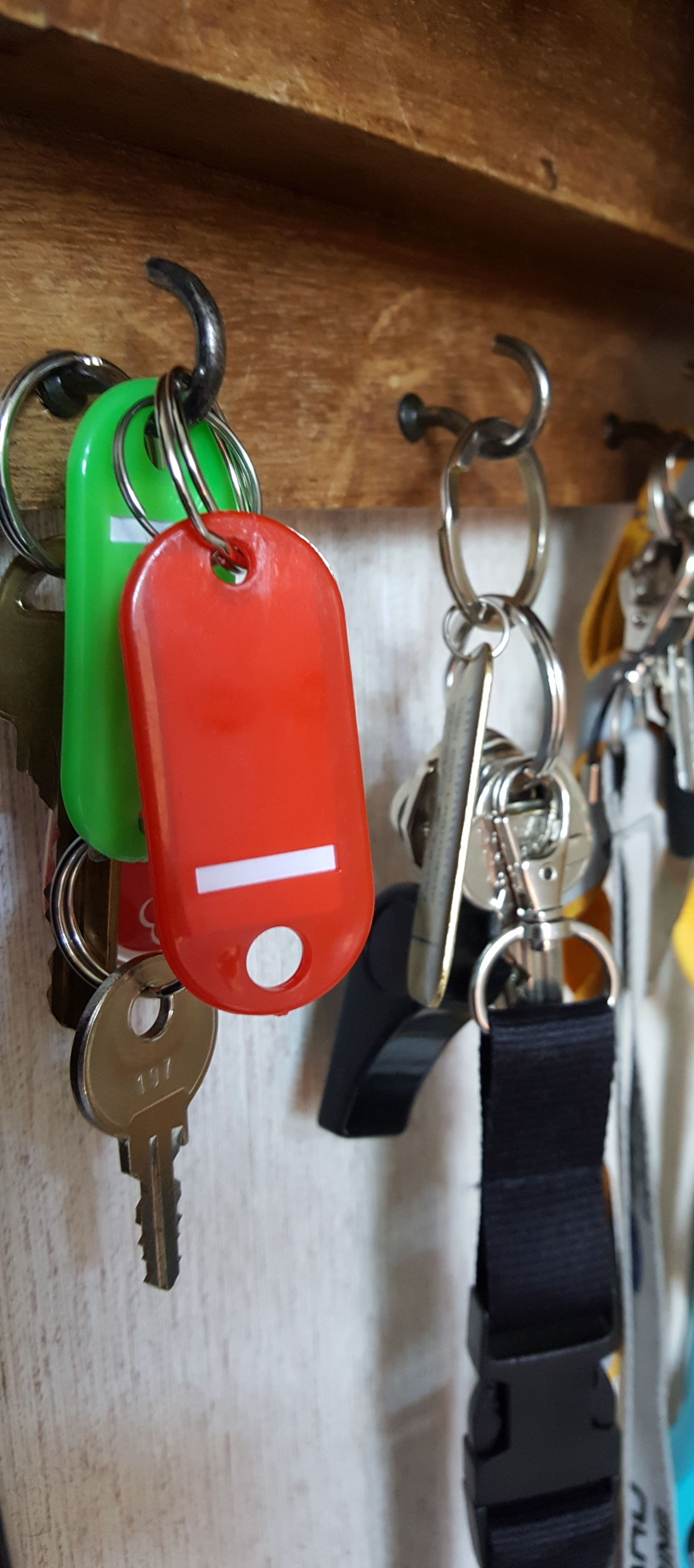 Colorful keys and key fobs hanging on hooks indoors, including a red tag and black lanyard.