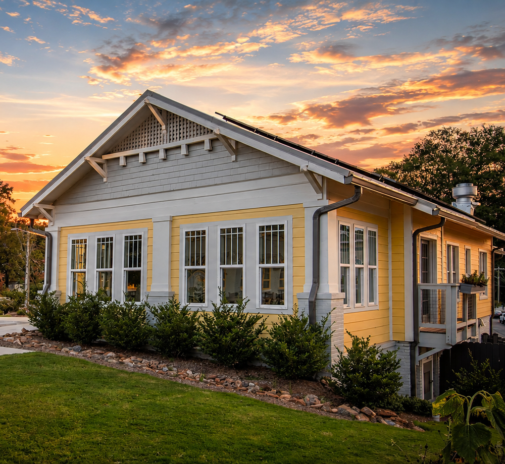 Yellow cottage with white trim and flower boxes at sunset, surrounded by a green lawn.