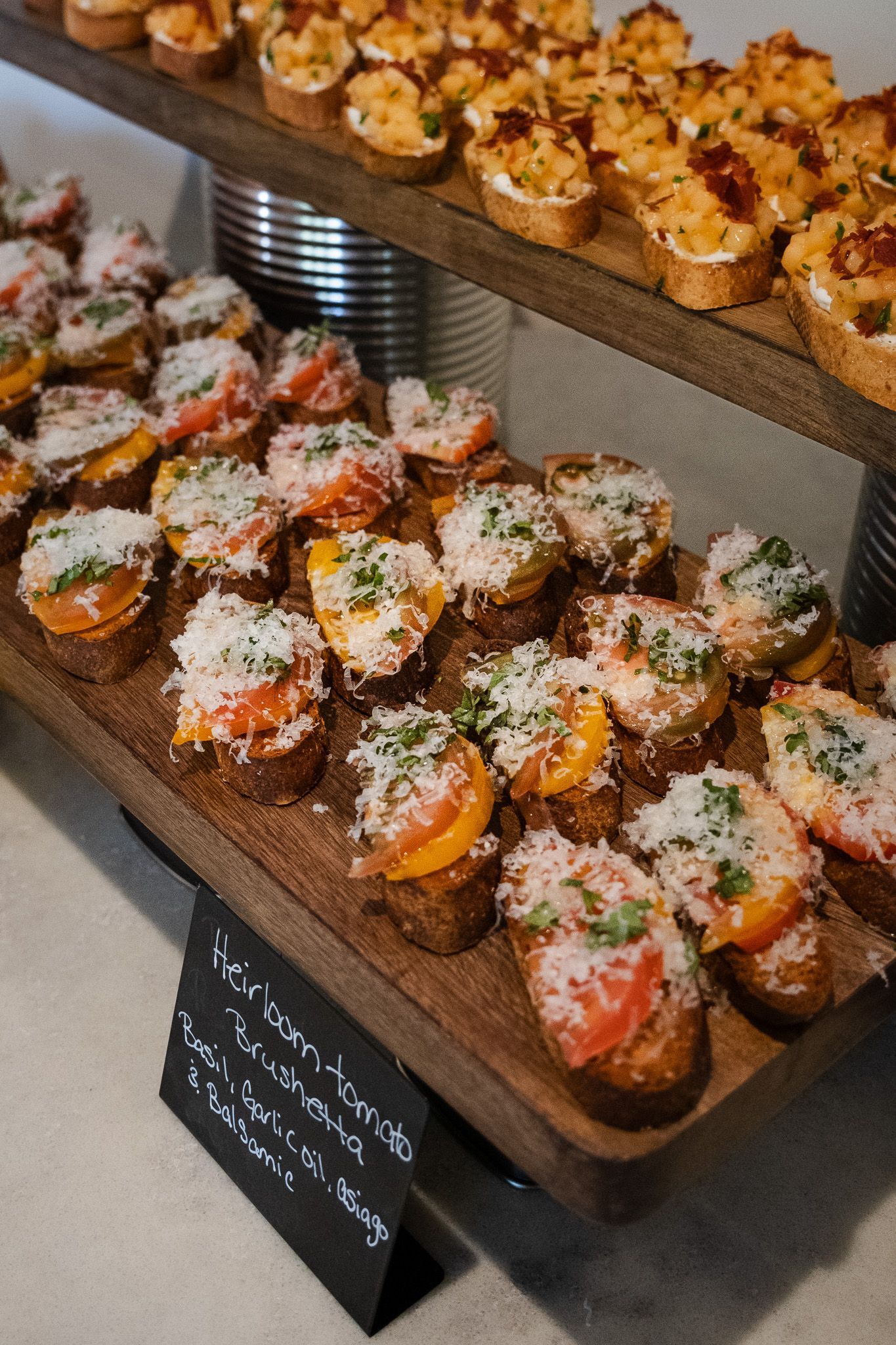 A tray of assorted bruschetta topped with tomatoes, cheese, and herbs on a wooden display shelf