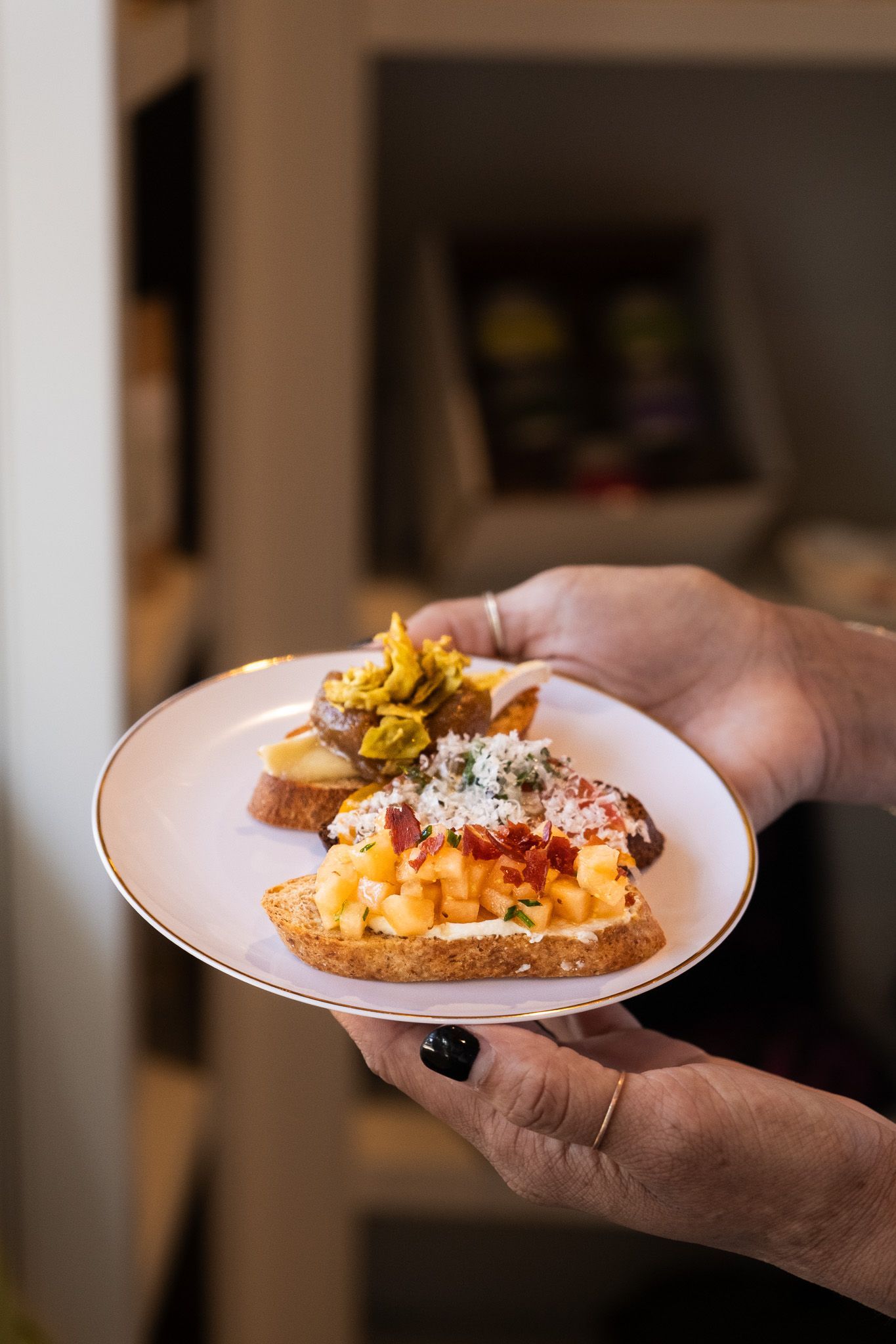 Hand holding a small white plate with a plated gourmet appetizer garnished with herbs and vegetables