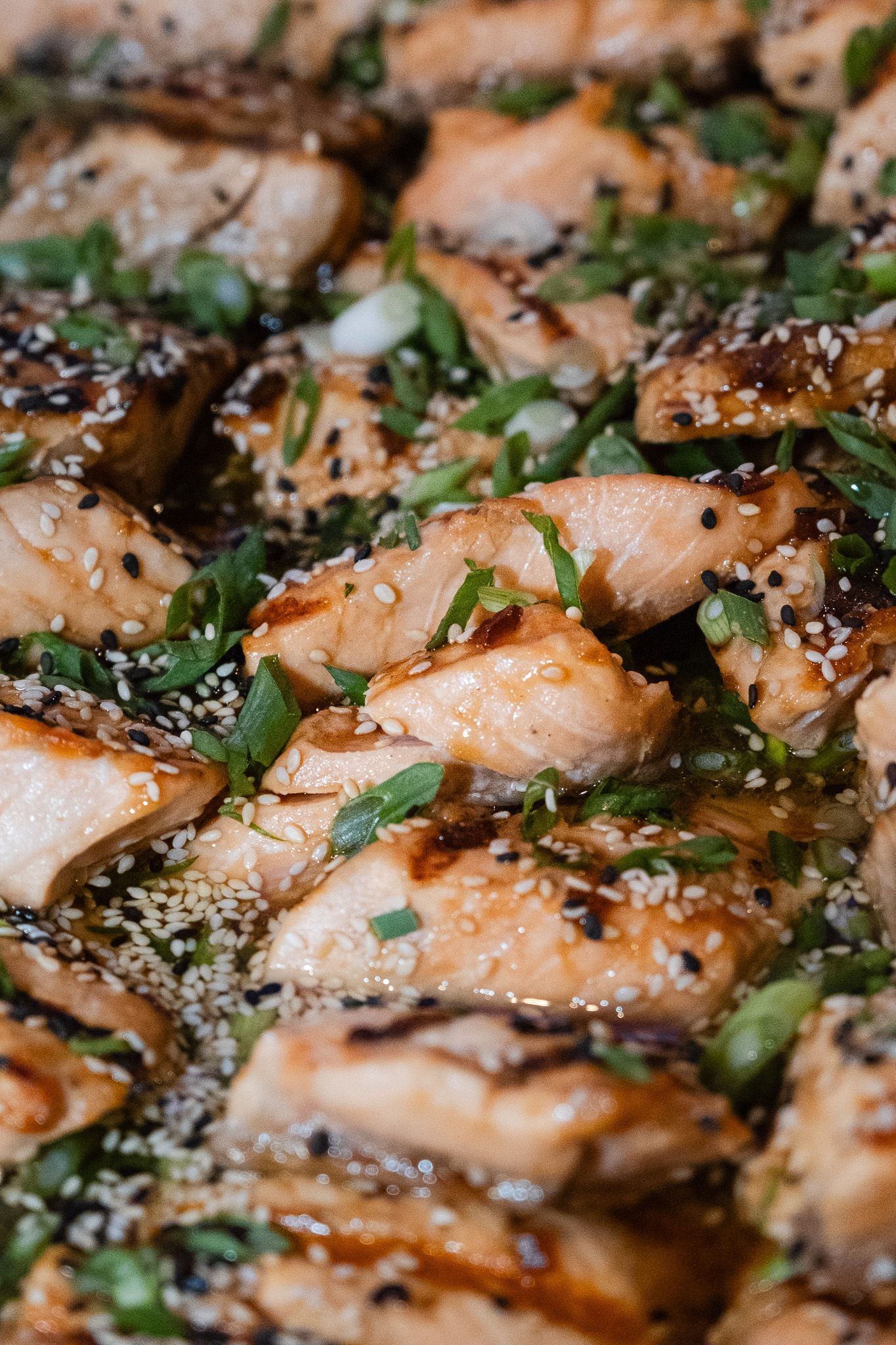Grilled chicken pieces topped with chopped herbs and black sesame seeds on a pan