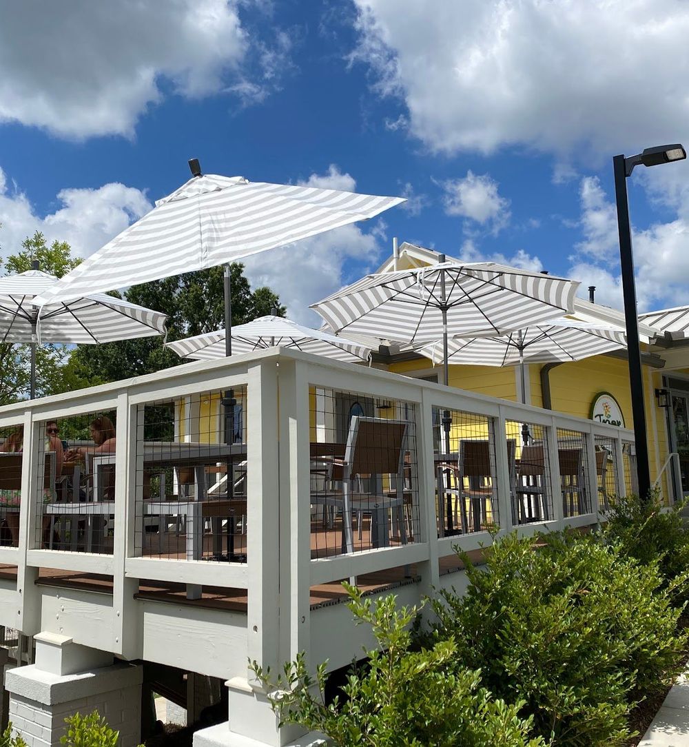 White outdoor patio with umbrellas, chairs, and glass railings under a blue sky with clouds