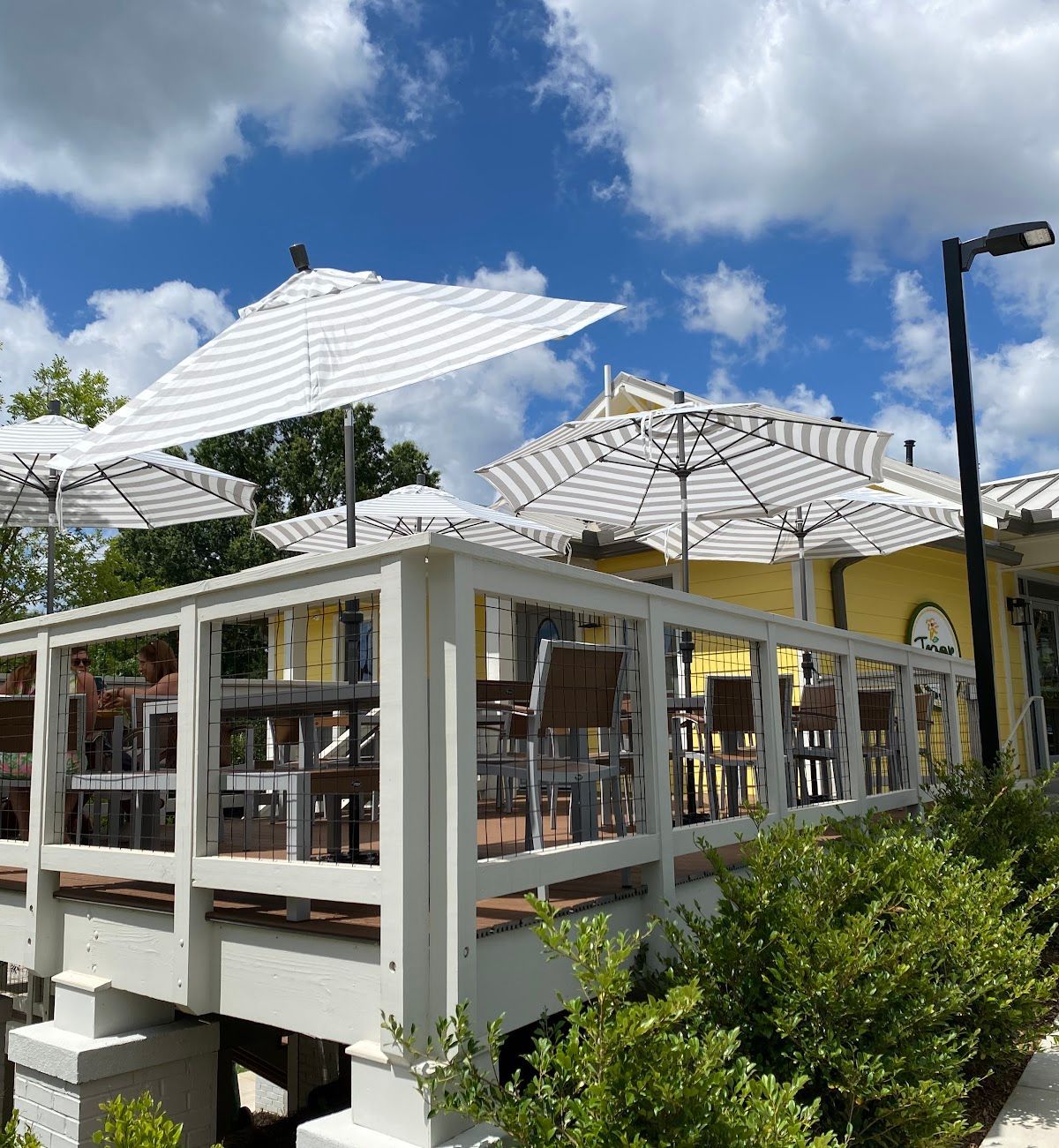 White outdoor patio with umbrellas, chairs, and glass railings under a blue sky with clouds