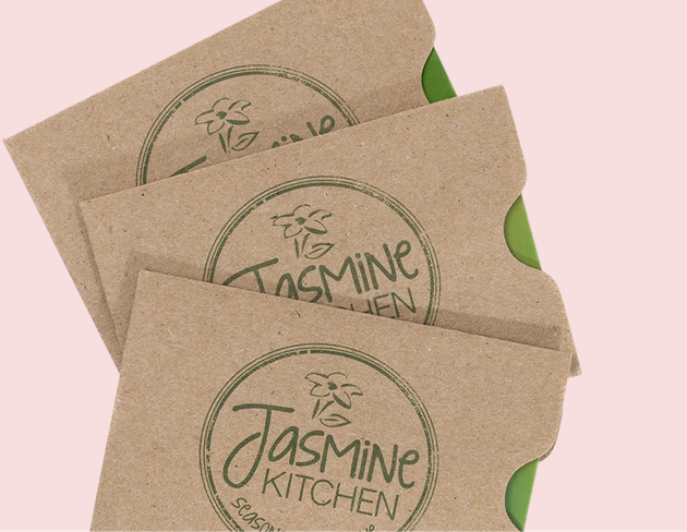 Three stacked brown Jasmine Kitchen paper bags on a pale pink background