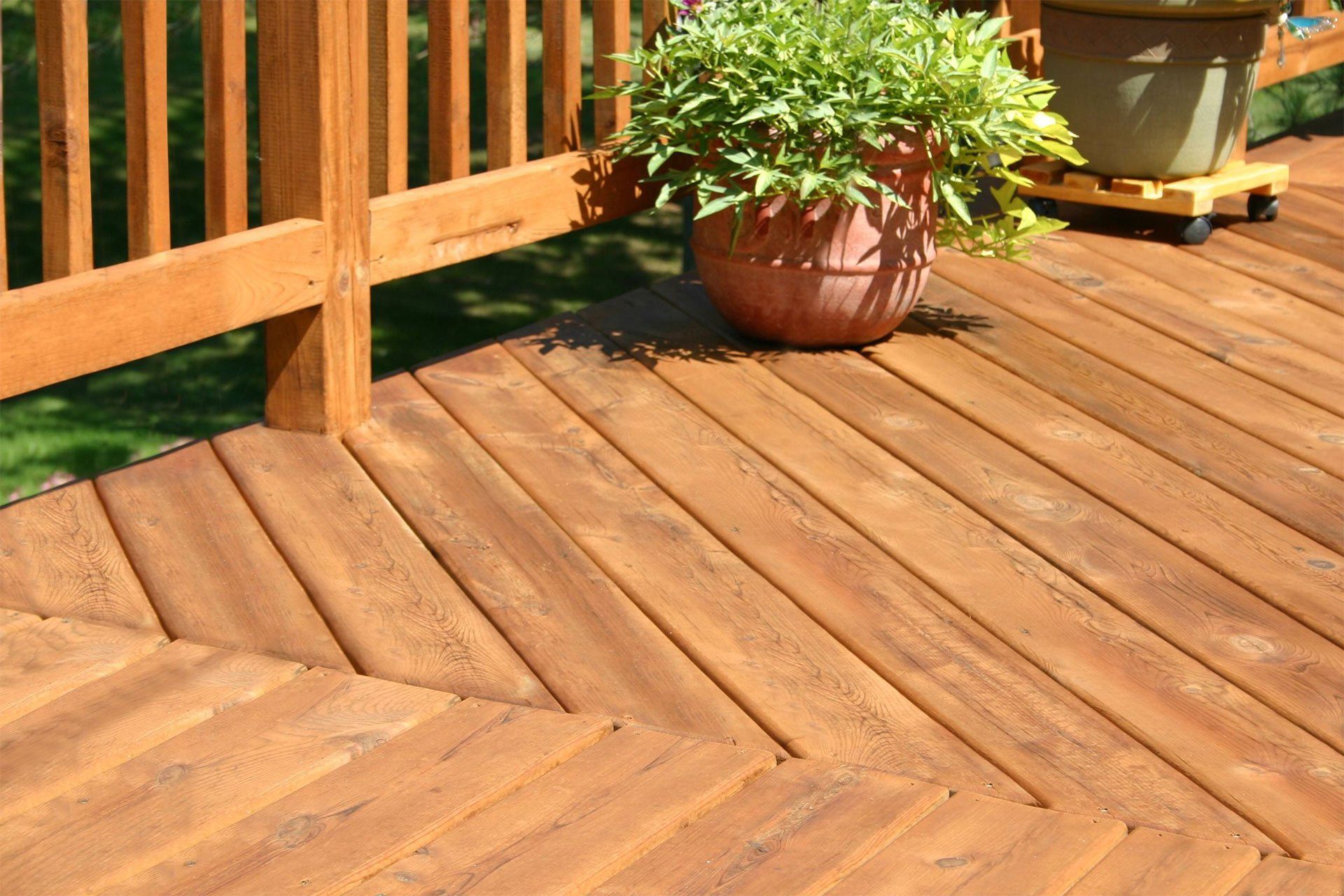 Wooden deck with reddish-brown planks and railing, featuring potted plants in the corner.