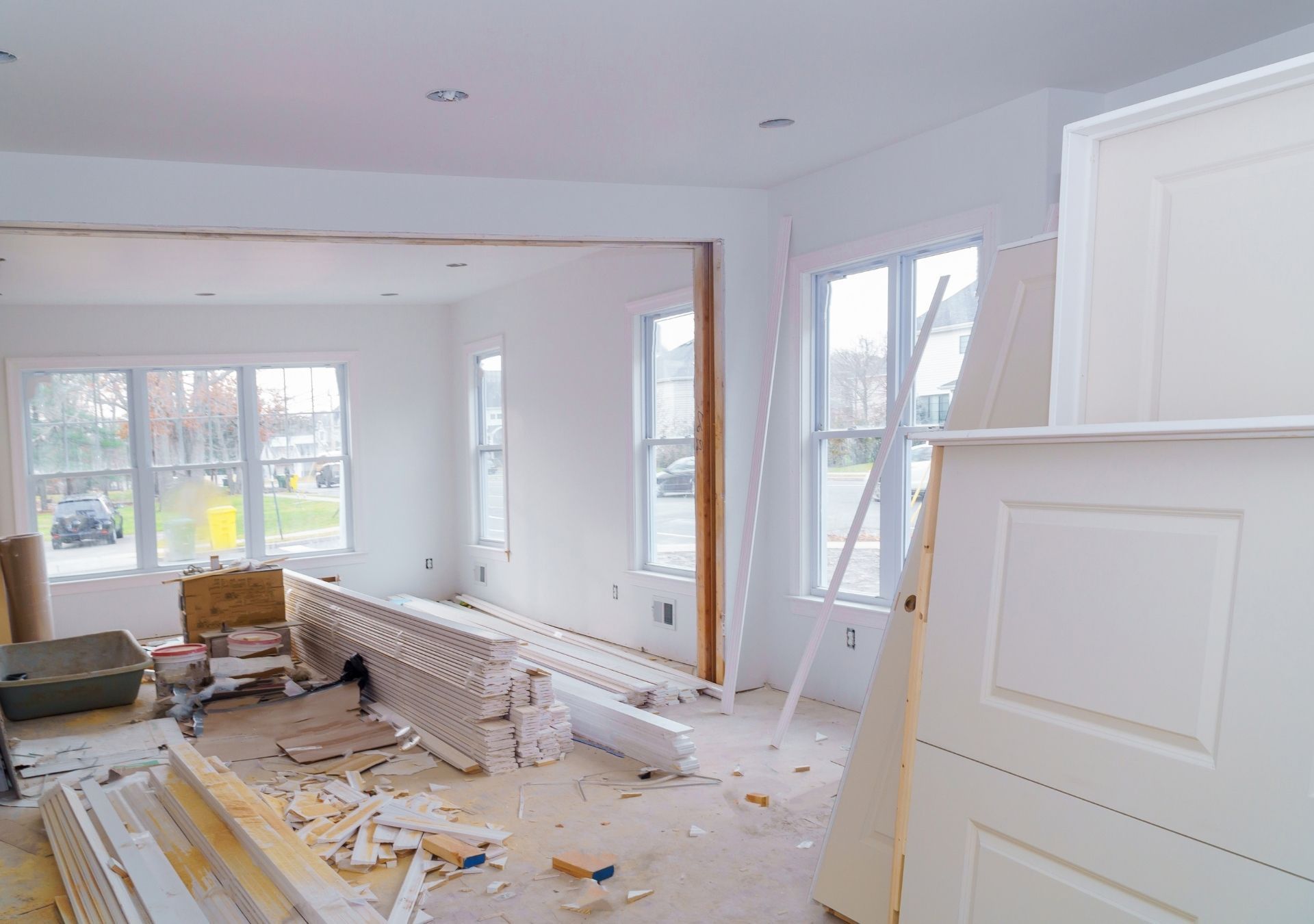 Interior of a room under renovation; white walls, windows, debris, and materials are visible.