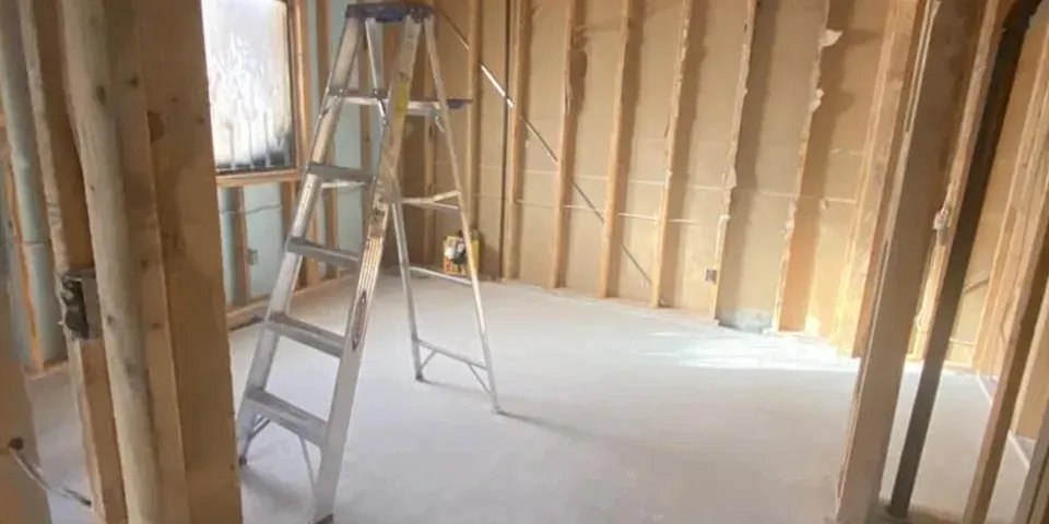 Ladders in an unfinished room with exposed wall framing and a bare floor.