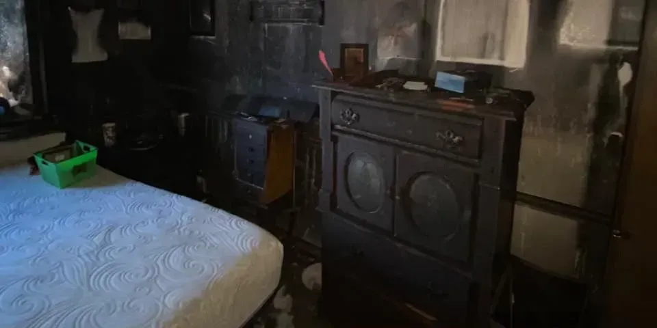 Dim bedroom with a bed, black dresser, and a small green toy on the bed.
