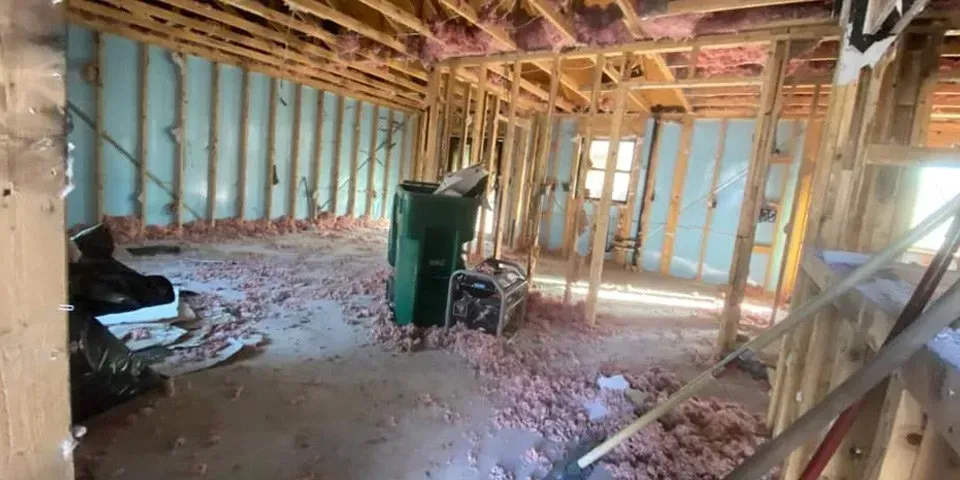 Partially framed room under construction with exposed studs, insulation, debris, and a green trash bin
