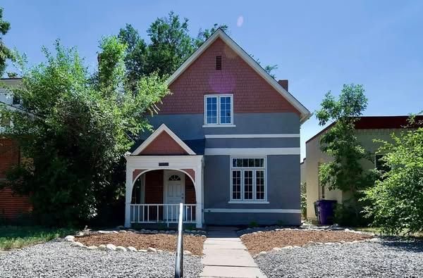 Blue and brick two-story house with a small front porch, flanked by trees and a short walkway.
