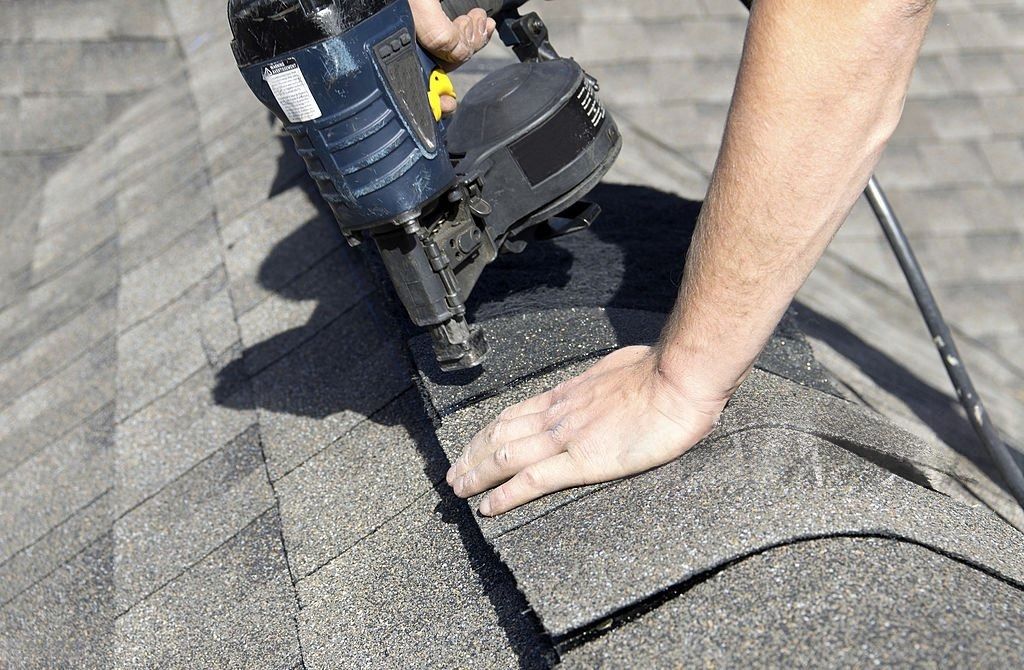 Person uses a nail gun to fasten shingles to a roof.